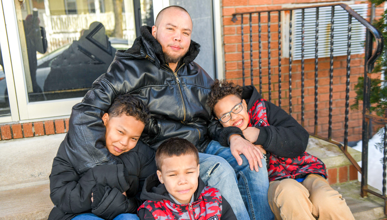Father sits with sons on porch steps of brick building